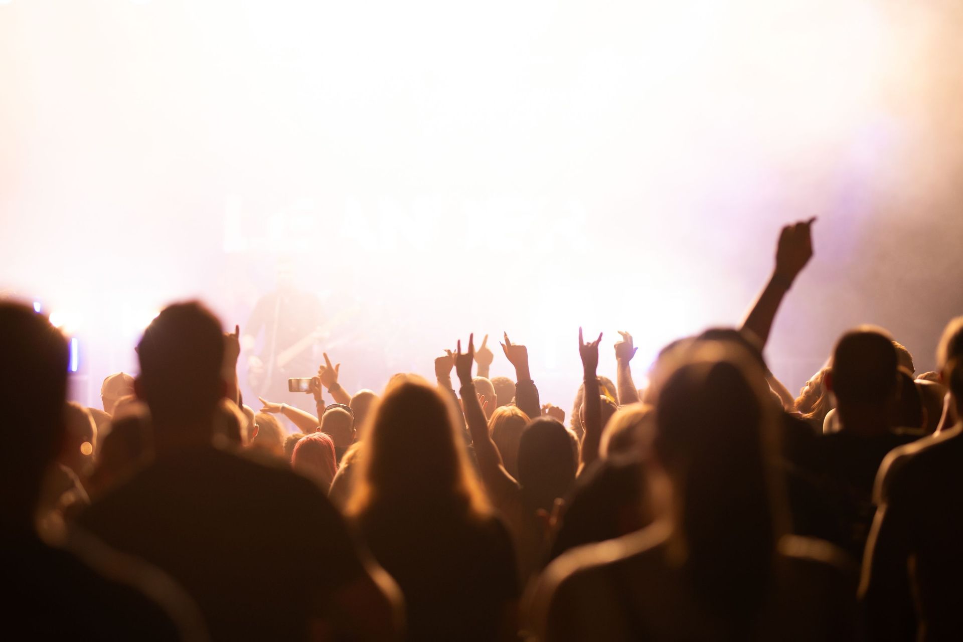 A crowd at a Club SEEN headline event, hands raised toward a brightly lit stage